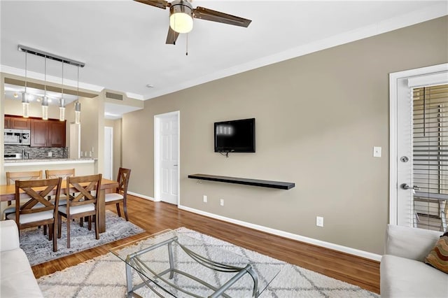 living area featuring visible vents, wood finished floors, ceiling fan, and crown molding