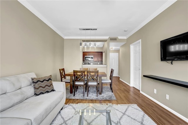 living area with visible vents, wood finished floors, baseboards, and ornamental molding