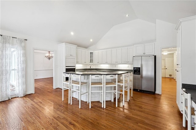 kitchen featuring stainless steel fridge, backsplash, hardwood / wood-style floors, a kitchen breakfast bar, and white cabinets