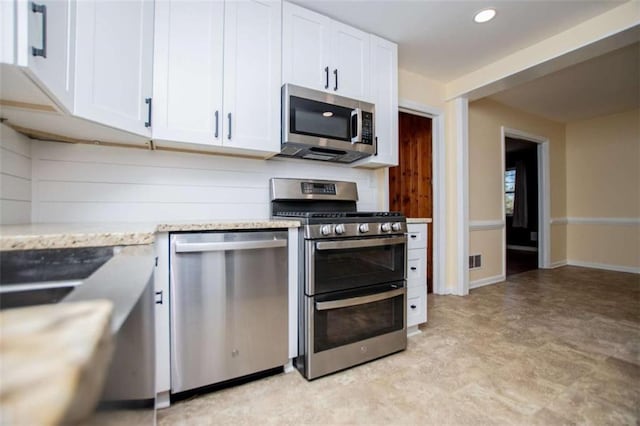 kitchen with stainless steel appliances, light stone countertops, and white cabinets