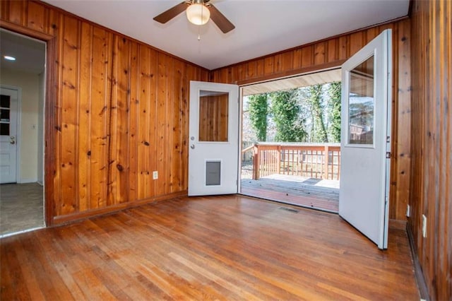 doorway with hardwood / wood-style flooring, wooden walls, and ceiling fan