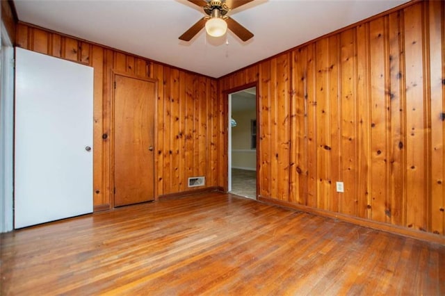 empty room with ceiling fan, wood walls, and light wood-type flooring