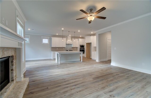 unfurnished living room featuring a ceiling fan, a brick fireplace, crown molding, and light wood finished floors