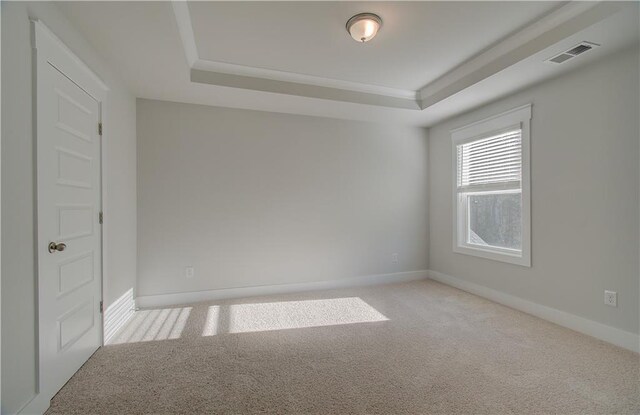 carpeted empty room featuring visible vents, baseboards, a tray ceiling, and ornamental molding