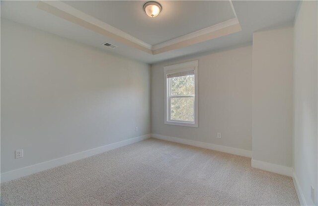 spare room featuring visible vents, a tray ceiling, crown molding, baseboards, and light colored carpet