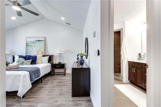 bedroom featuring visible vents, ensuite bath, light wood finished floors, baseboards, and vaulted ceiling