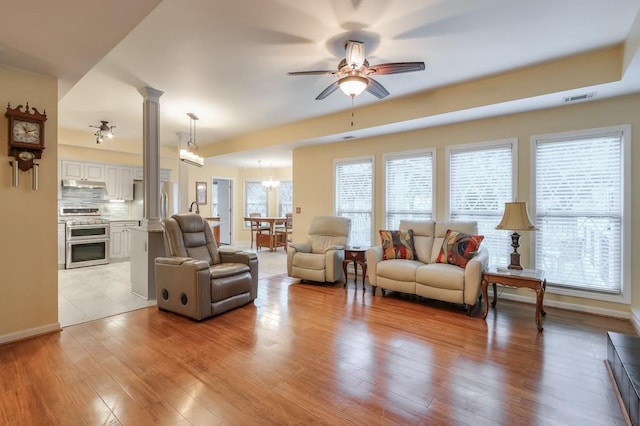 living room featuring ceiling fan with notable chandelier, light hardwood / wood-style floors, and decorative columns