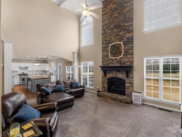 carpeted living room featuring a stone fireplace, ceiling fan, and a high ceiling