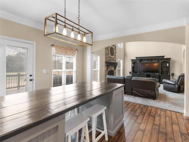 kitchen featuring a fireplace, wooden counters, hanging light fixtures, ornamental molding, and dark wood-type flooring