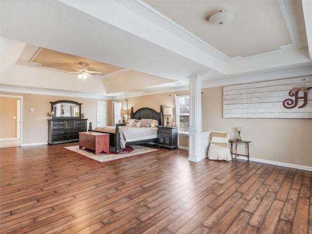 bedroom with dark wood-type flooring, a tray ceiling, crown molding, and ornate columns