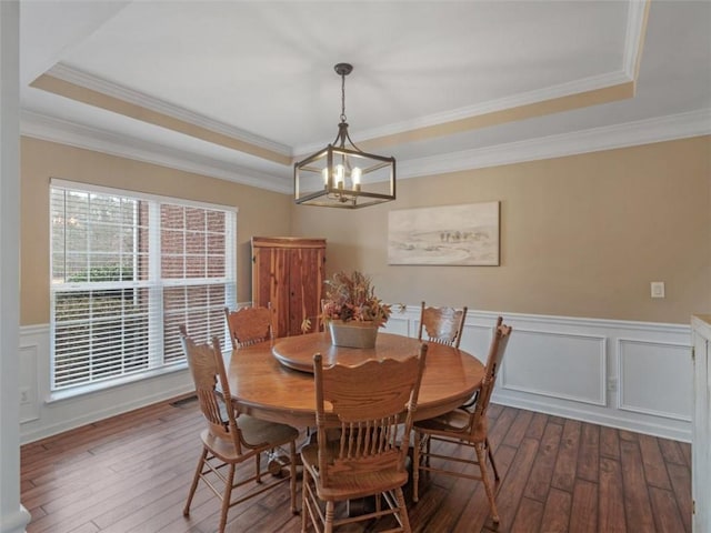 dining area with an inviting chandelier, a tray ceiling, dark wood-type flooring, and ornamental molding