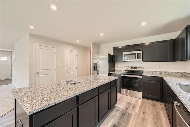 kitchen with a sink, light wood-type flooring, light stone countertops, appliances with stainless steel finishes, and a kitchen island