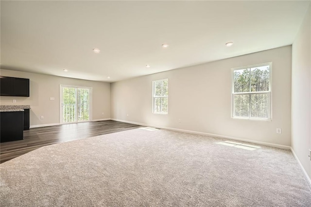 unfurnished living room featuring dark colored carpet, baseboards, a healthy amount of sunlight, and recessed lighting