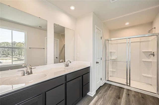 bathroom featuring double vanity, wood finished floors, a stall shower, and a sink
