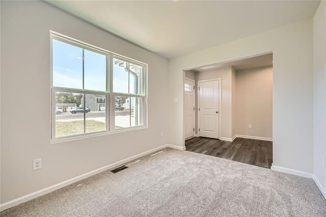 unfurnished room with baseboards, visible vents, and dark carpet