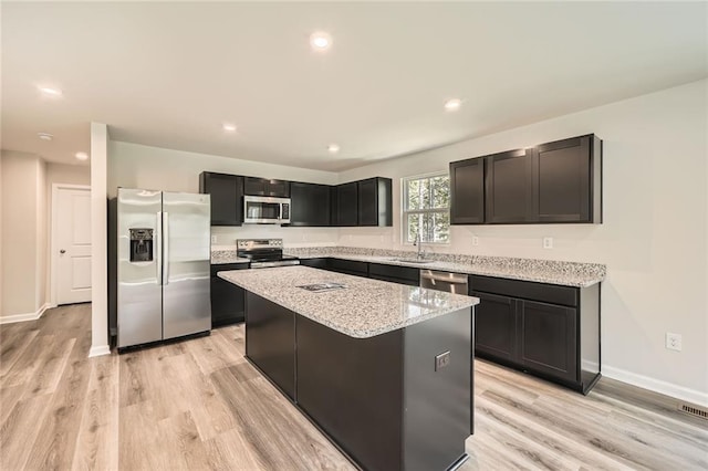 kitchen featuring a center island, light wood-type flooring, stainless steel appliances, and light stone countertops