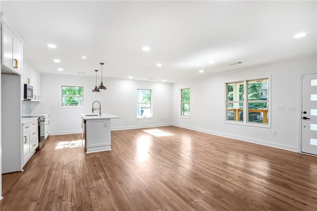 unfurnished living room featuring a sink, healthy amount of natural light, wood finished floors, recessed lighting, and baseboards