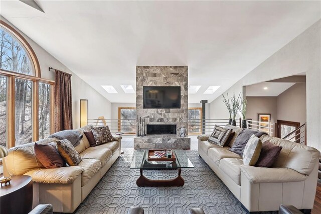 living area featuring a stone fireplace and lofted ceiling with skylight