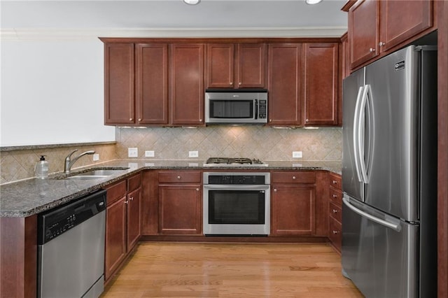 kitchen with sink, light wood-type flooring, dark stone countertops, ornamental molding, and stainless steel appliances