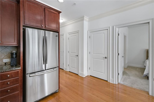 kitchen featuring crown molding, light wood-type flooring, backsplash, and stainless steel refrigerator