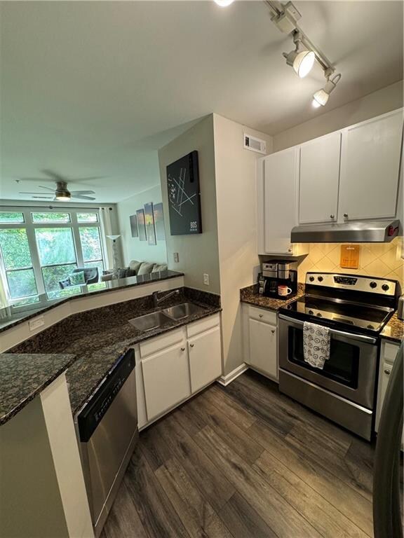 kitchen featuring dark hardwood / wood-style floors, appliances with stainless steel finishes, ceiling fan, dark stone counters, and rail lighting