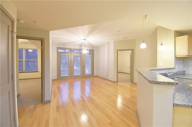 interior space with pendant lighting, light wood-type flooring, light stone counters, a peninsula, and a sink