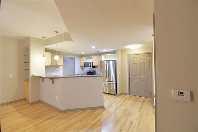 kitchen featuring light stone counters, light wood finished floors, a peninsula, appliances with stainless steel finishes, and decorative light fixtures