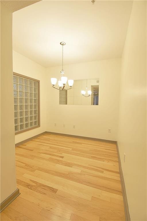 empty room featuring baseboards, light wood-style floors, and a chandelier