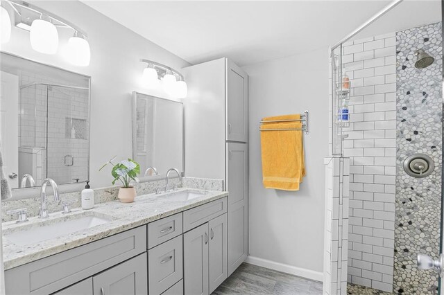 bathroom featuring baseboards, a sink, double vanity, and a stall shower