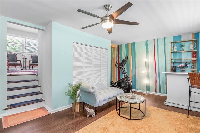 sitting room featuring baseboards, wallpapered walls, a ceiling fan, wood finished floors, and stairway