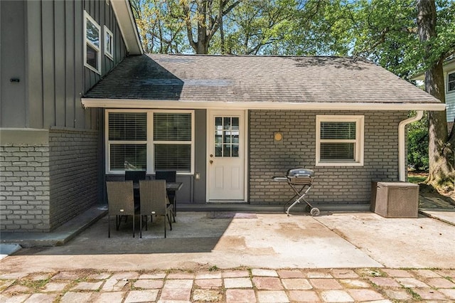 property entrance with board and batten siding, a patio area, a shingled roof, and brick siding