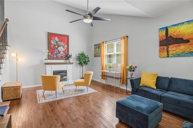 living area with a glass covered fireplace, wood finished floors, a ceiling fan, and high vaulted ceiling