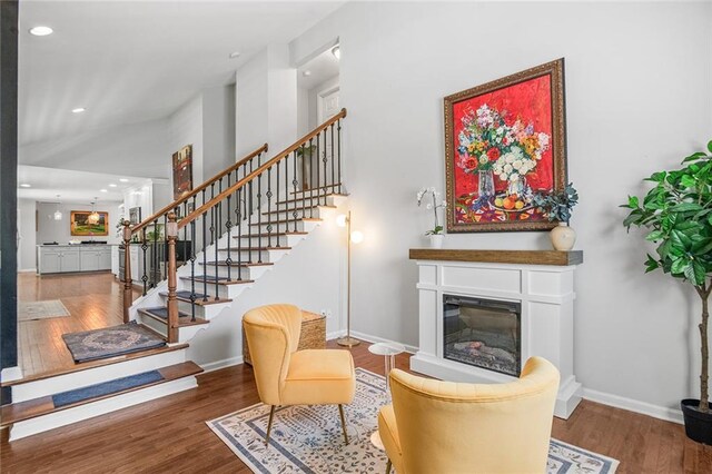 living area featuring stairway, wood finished floors, a glass covered fireplace, baseboards, and recessed lighting