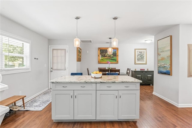 kitchen featuring light stone counters, wood finished floors, a kitchen island, pendant lighting, and baseboards