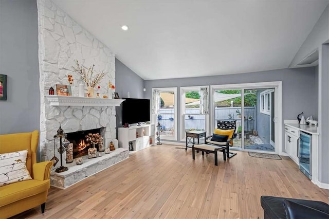 living room with a fireplace, beverage cooler, vaulted ceiling, and light hardwood / wood-style flooring