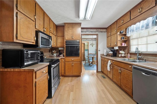 kitchen with appliances with stainless steel finishes, sink, light hardwood / wood-style flooring, and a textured ceiling