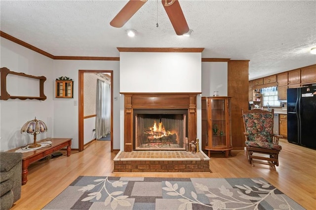 living room with a brick fireplace, crown molding, a textured ceiling, and light wood-type flooring