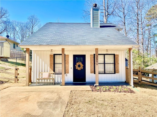 view of front of home with covered porch, board and batten siding, a chimney, and fence