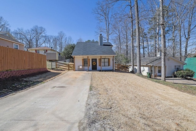 view of front of house with driveway, a chimney, fence, and roof with shingles