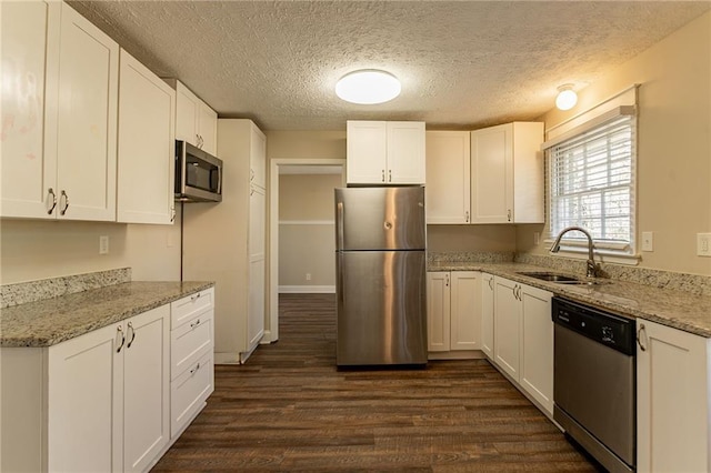 kitchen with light stone countertops, white cabinetry, sink, stainless steel appliances, and a textured ceiling