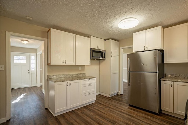 kitchen with white cabinets, appliances with stainless steel finishes, dark hardwood / wood-style floors, and light stone countertops