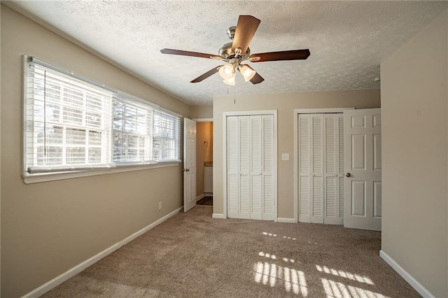 unfurnished bedroom with a textured ceiling, ceiling fan, carpet, and two closets