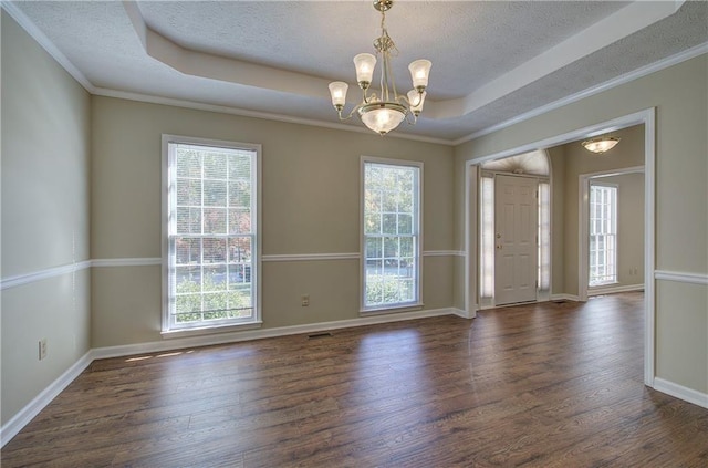 empty room featuring a chandelier, a raised ceiling, plenty of natural light, and wood finished floors