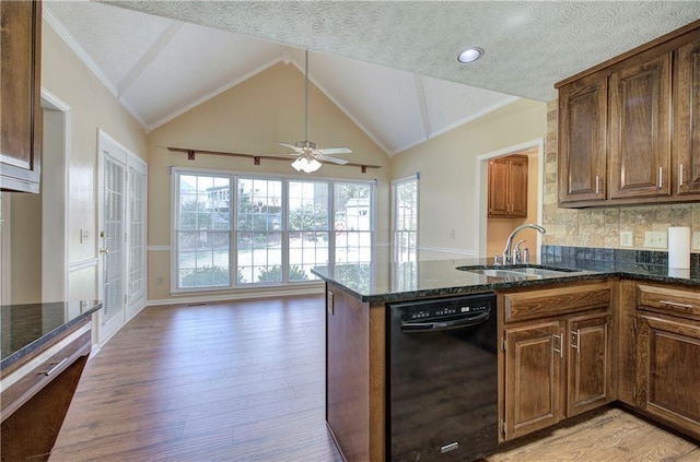 kitchen with black dishwasher, dark stone counters, lofted ceiling, light wood-style floors, and a sink