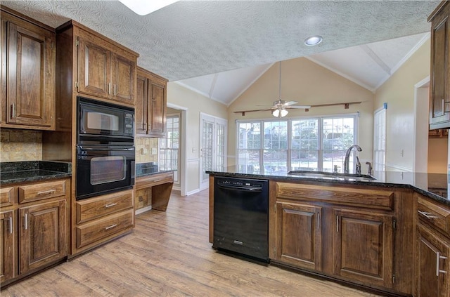 kitchen with lofted ceiling, a sink, light wood-style floors, dark stone counters, and black appliances