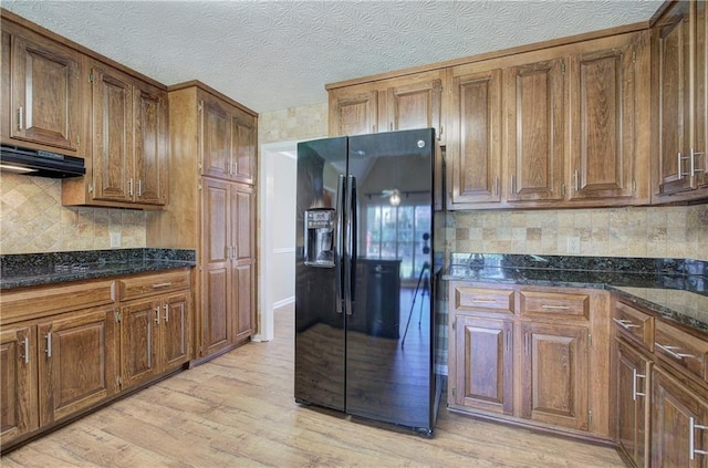 kitchen featuring a textured ceiling, under cabinet range hood, black fridge, light wood-type flooring, and tasteful backsplash