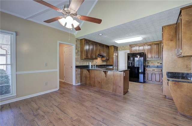 kitchen with a peninsula, under cabinet range hood, light wood-style flooring, and black fridge