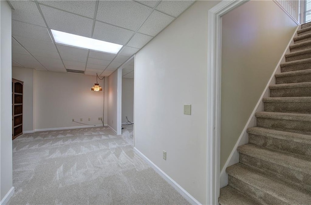 basement featuring a paneled ceiling, light carpet, stairway, and baseboards