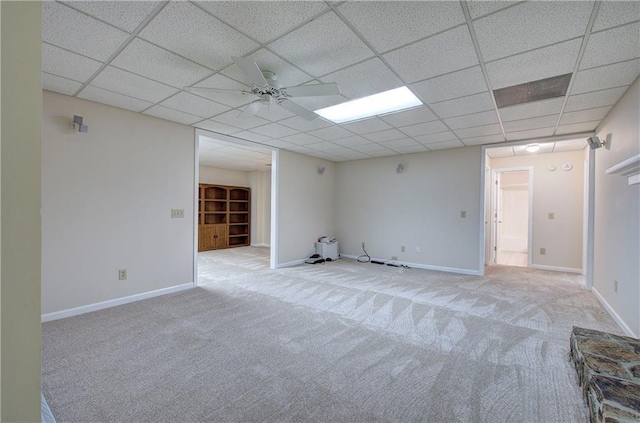 carpeted spare room featuring a drop ceiling, ceiling fan, and baseboards