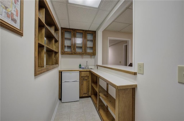 bar with refrigerator, light tile patterned floors, a sink, a drop ceiling, and baseboards